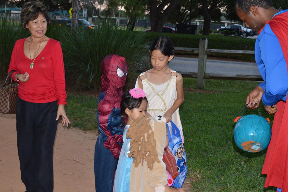 Kid dressed as Spiderman stands with girl dressed in Greek-style dress, girl dressed in blue princess outfit and child dressed as lion and man dressed as Superman